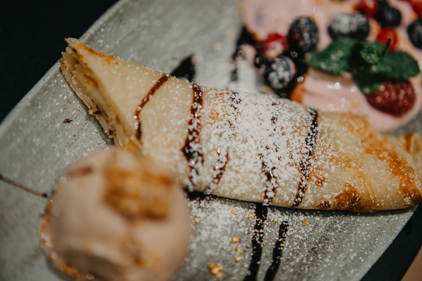 Ein hübsch angerichteter gerollter Pfannkuchen mit Eis, Früchten und Puderzucker
